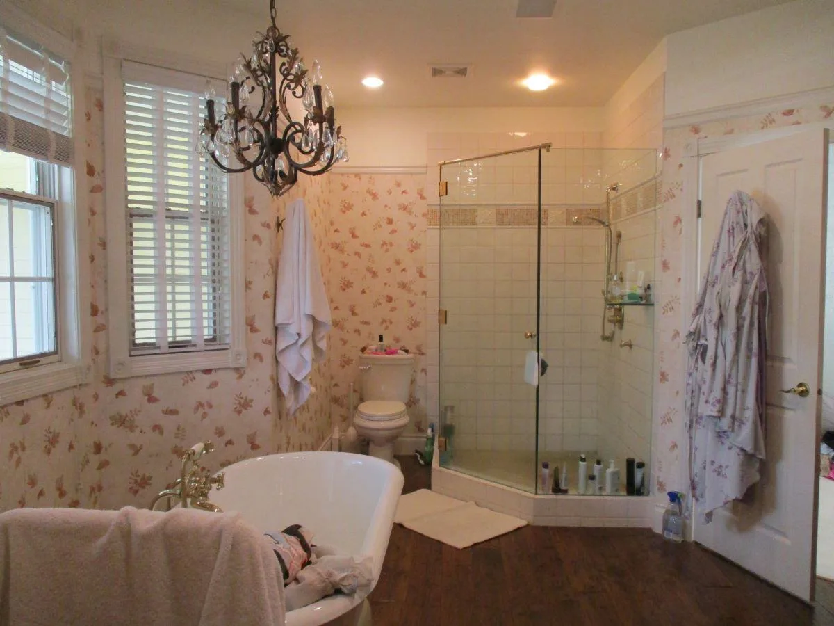 Avant : salle de bains avec baignoire, douche vitrée, papier peint fleuri et sol sombre.