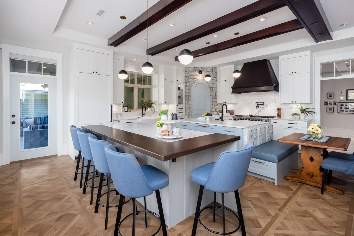 Après : cuisine blanche et bleu clair, îlot avec assises bleues, banquette et poutres foncées.